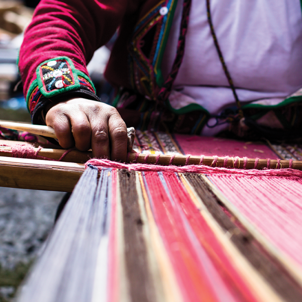 An indigenous person weaving colorful fabric.