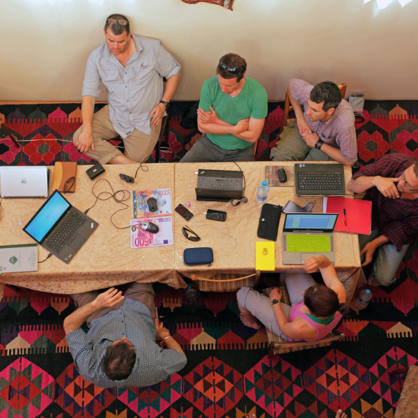 A team of six archeologists sitting around a table participating in a discussion.