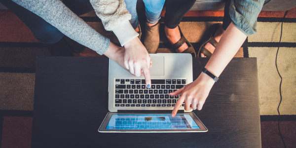 three students gesturing to the screen of a laptop